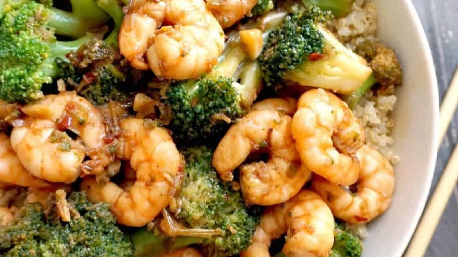 A bowl containing cooked shrimp, broccoli florets, and a sauce, served over grains.