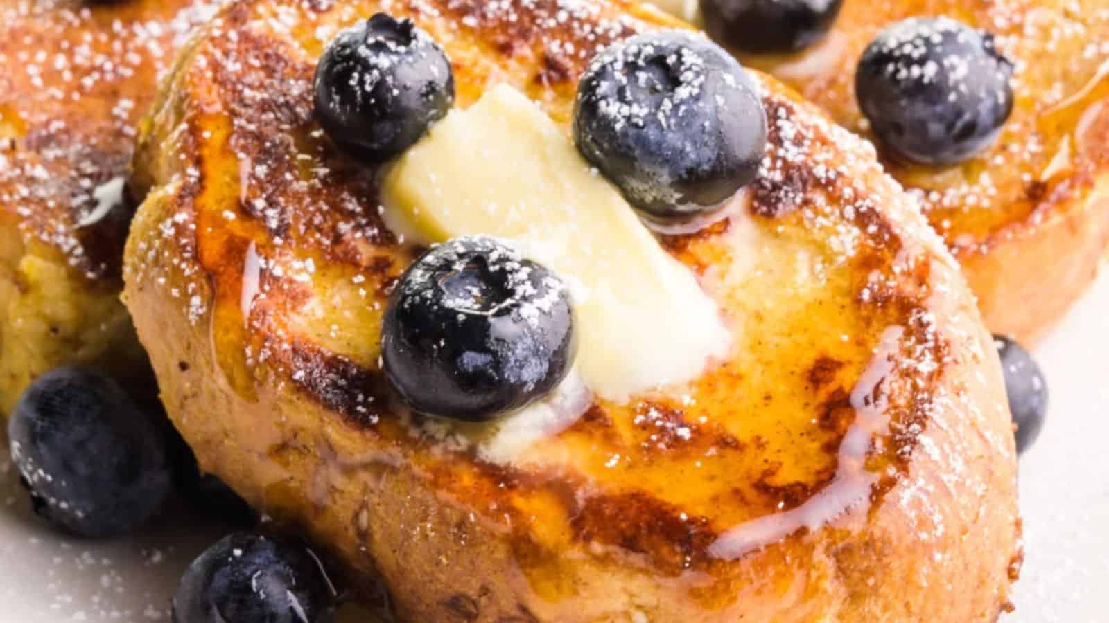 Slices of French toast topped with blueberries, a pat of butter, powdered sugar, and syrup.