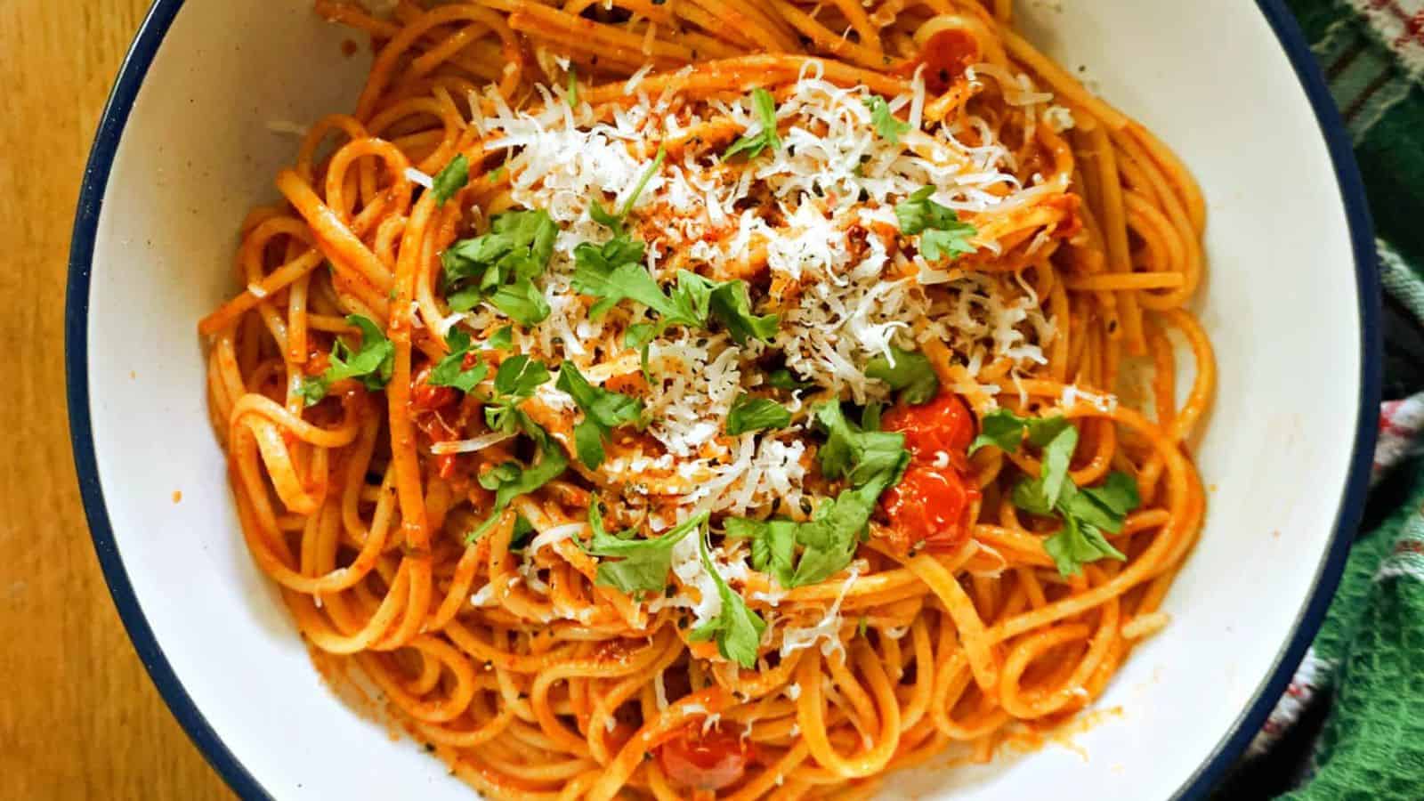 A bowl of spaghetti with tomato sauce, grated cheese, chopped parsley, and cherry tomatoes, served on a white plate with a dark rim.