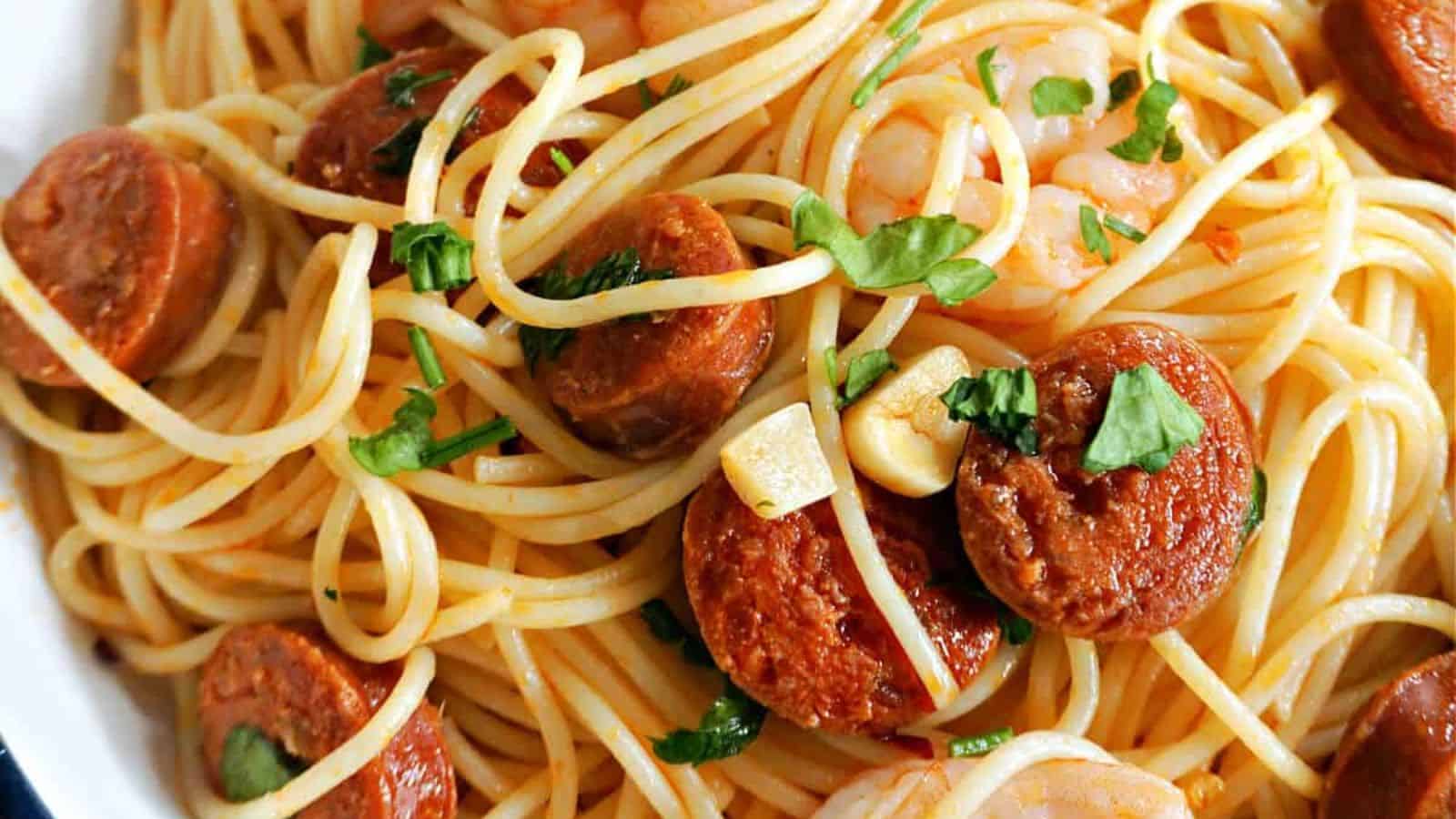 Spaghetti topped with sliced sausage, shrimp, garlic pieces, and chopped parsley.