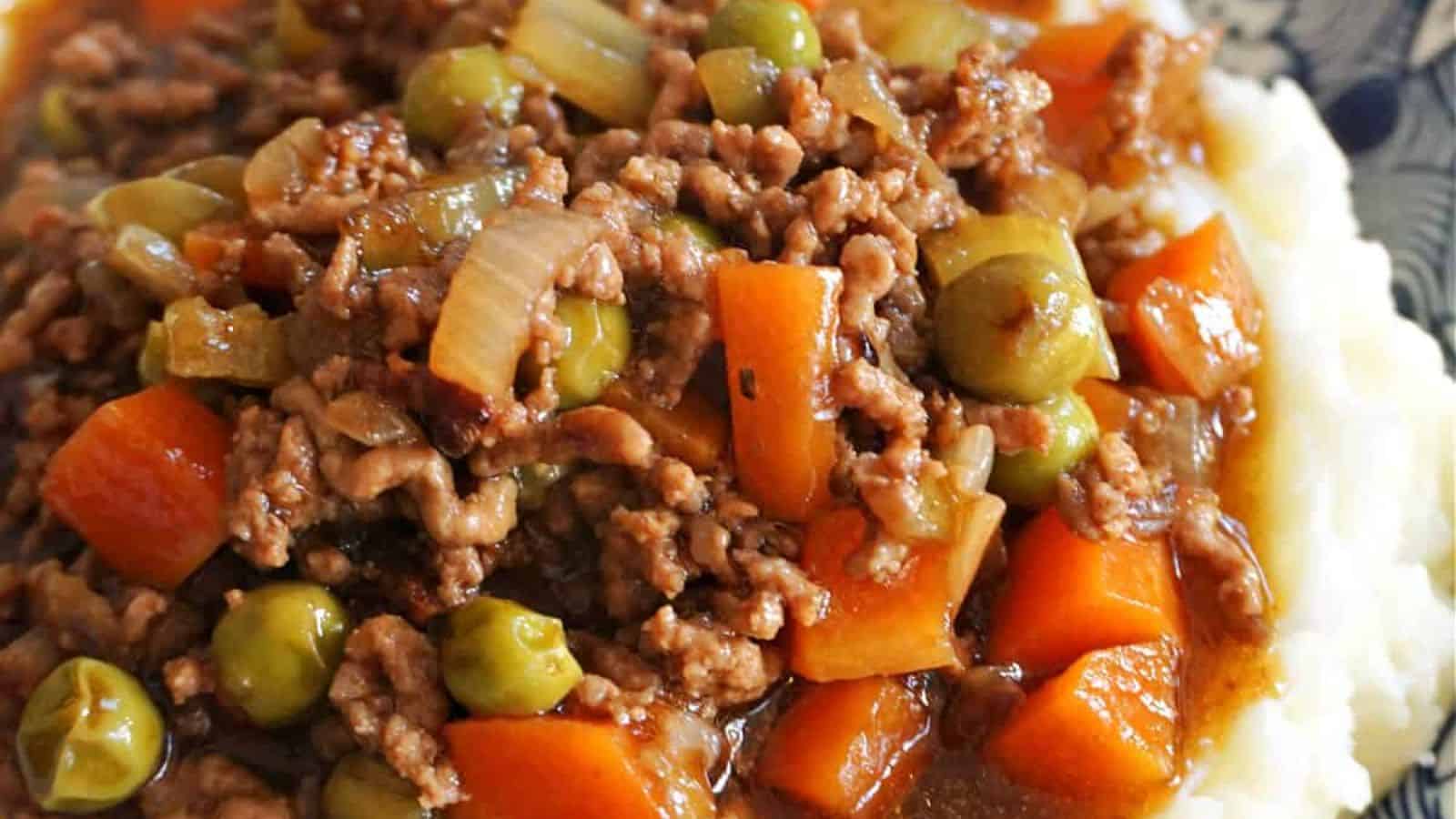 Ground beef stew with carrots, peas, and onions atop mashed potatoes.