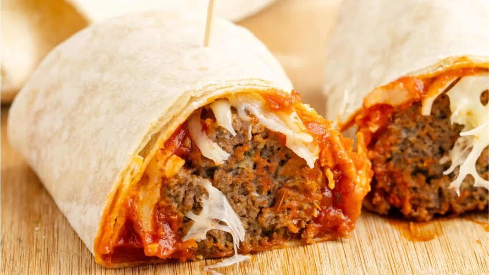 A halved tortilla wrap filled with meatballs, melted cheese, and tomato sauce, placed on a wooden surface.