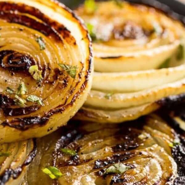 Grilled onion slices topped with chopped herbs on a dark plate.