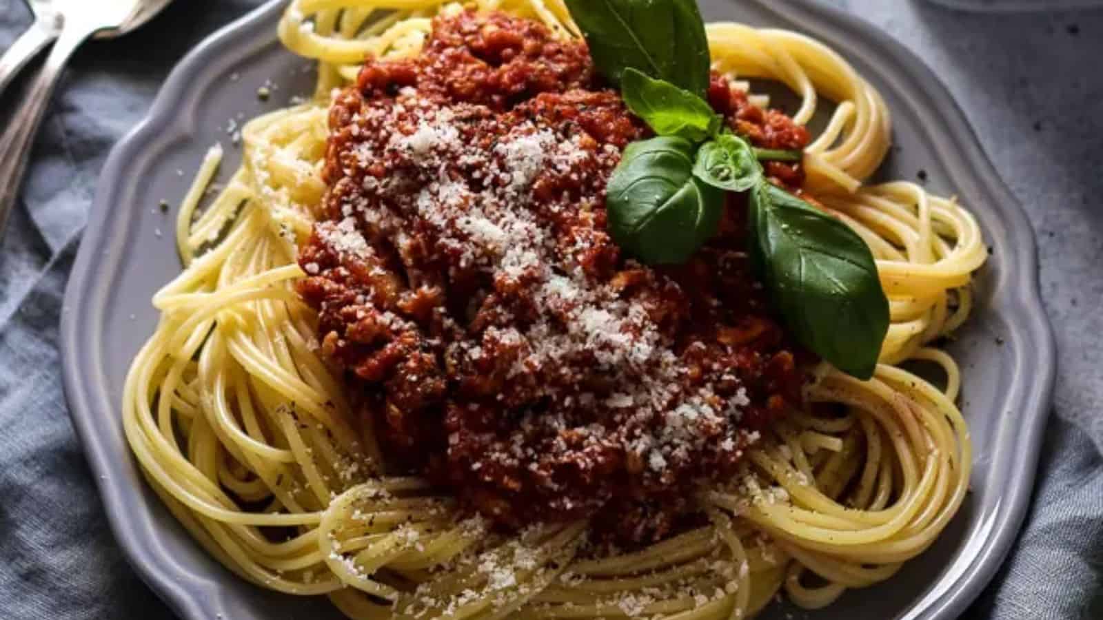 A plate of spaghetti with meat sauce, grated Parmesan cheese, and fresh basil leaves.