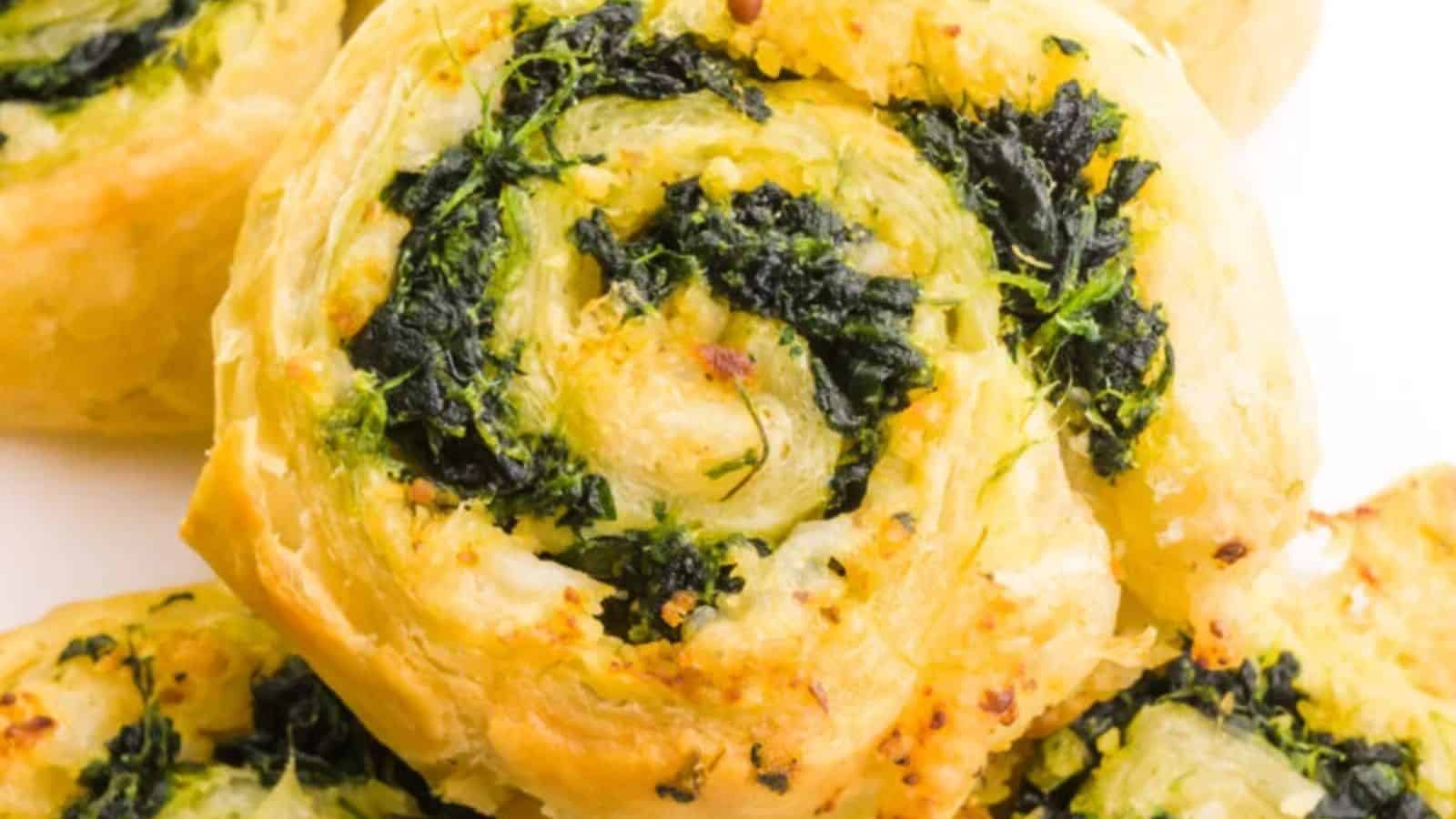 A golden-brown puff pastry pinwheel with visible layers, filled with green spinach and melted cheese.