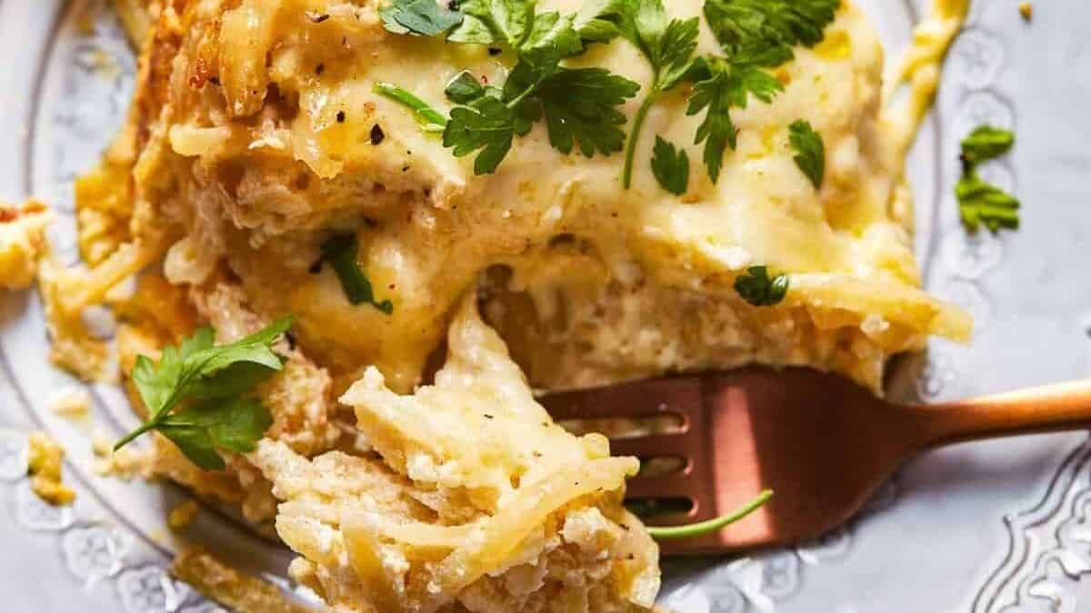 A serving of baked spaghetti casserole with melted cheese and chopped parsley on top, placed on a plate with a fork.