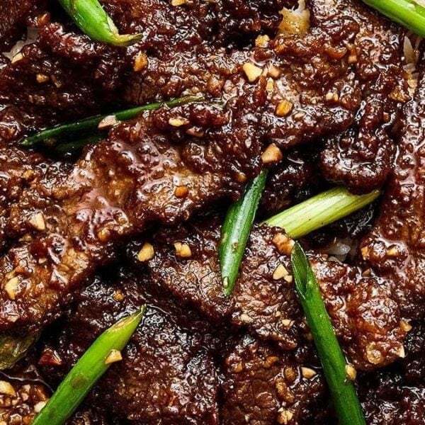 Slices of cooked beef with sauce, chopped garlic, and green onions served over white rice, accompanied by wooden chopsticks.