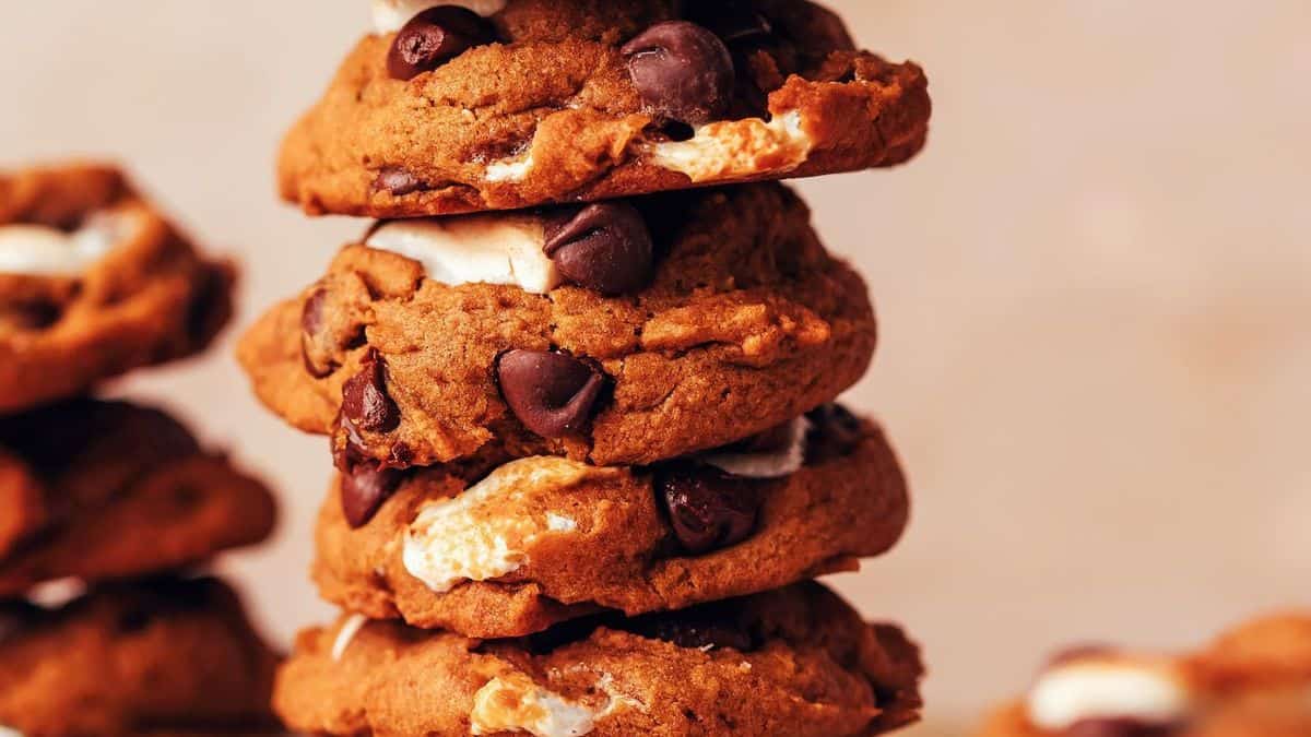 A stack of chocolate chip cookies with visible chunks of marshmallow, set against a blurred background.