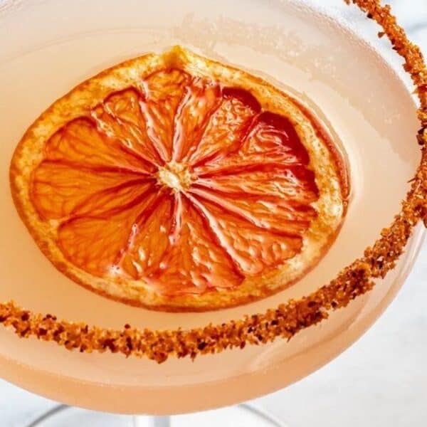 A glass filled with a bubbly drink, featuring a chili-rimmed edge and topped with a dried orange slice.