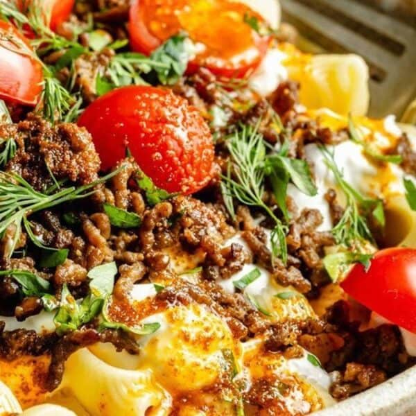 A ceramic bowl containing pasta topped with ground meat, halved cherry tomatoes, fresh green herbs, and a creamy white sauce.