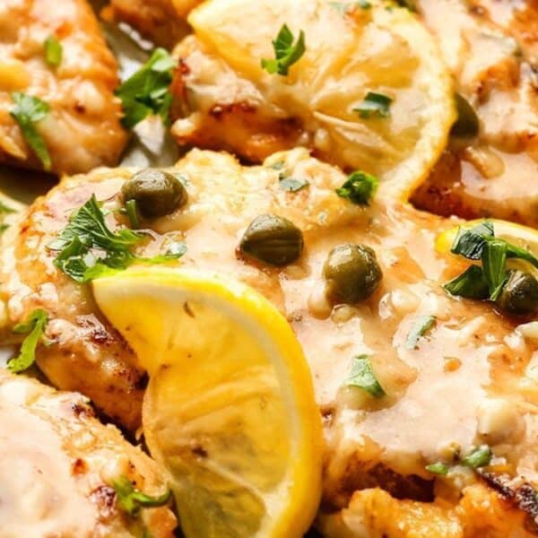 Chicken piccata topped with lemon slices, capers, and chopped parsley in a creamy sauce.