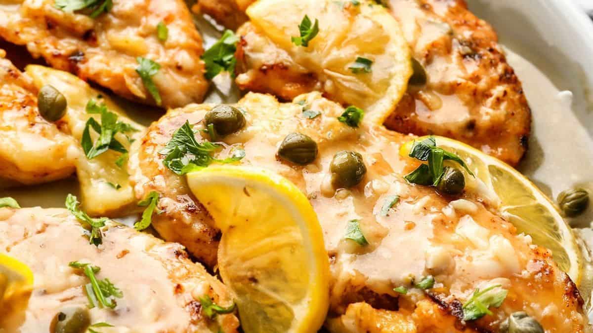 Chicken piccata topped with lemon slices, capers, and chopped parsley in a creamy sauce.