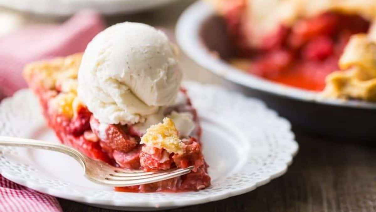 A slice of fruit pie topped with a scoop of vanilla ice cream sits on a white plate with a fork.