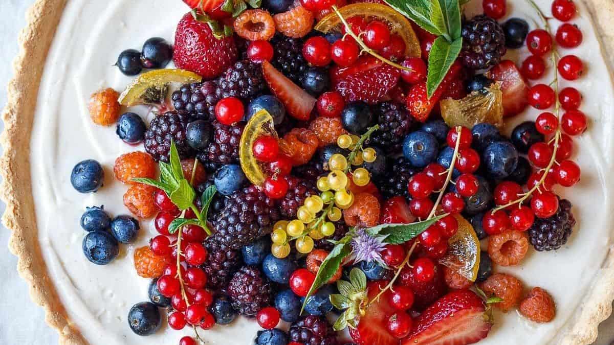 A tart topped with strawberries, blueberries, blackberries, red currants, and green leaves.