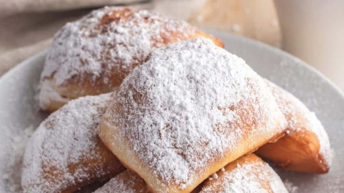 A plate with several golden-brown beignets topped with powdered sugar.