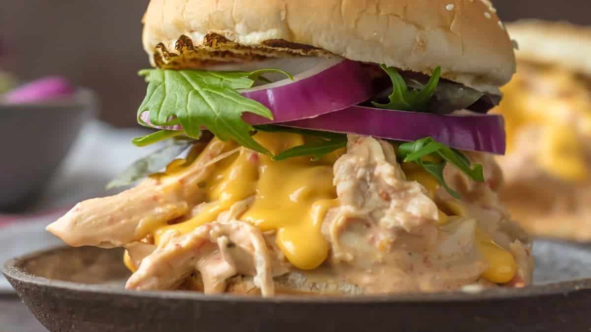 A sesame seed bun filled with melted cheese, leafy greens, red onion slices, and a chicken fillet.
