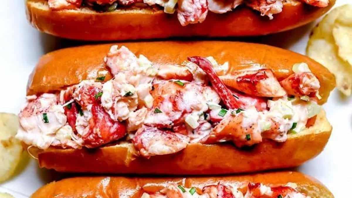 Three toasted buns filled with lobster meat, garnished with herbs, served alongside potato chips.