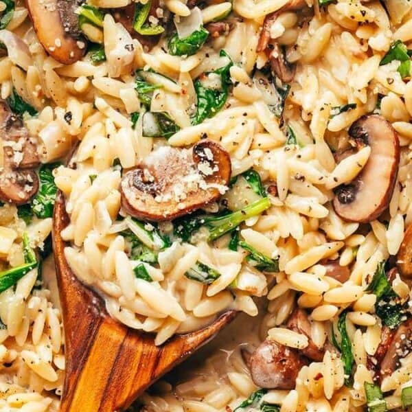 Cooked orzo pasta mixed with sautéed mushrooms and spinach, topped with sprinkled cheese, served in a skillet.