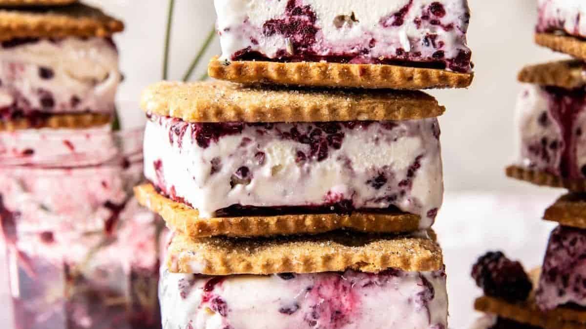 A stack of ice cream sandwiches made with graham cracker cookies and berry-filled ice cream; additional sandwiches and a jar appear in the background.