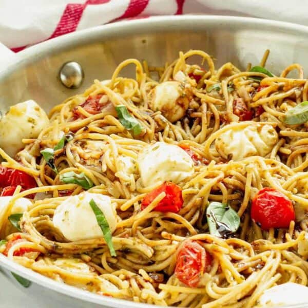 A skillet filled with spaghetti, cherry tomatoes, mozzarella balls, fresh basil, and a light sauce.