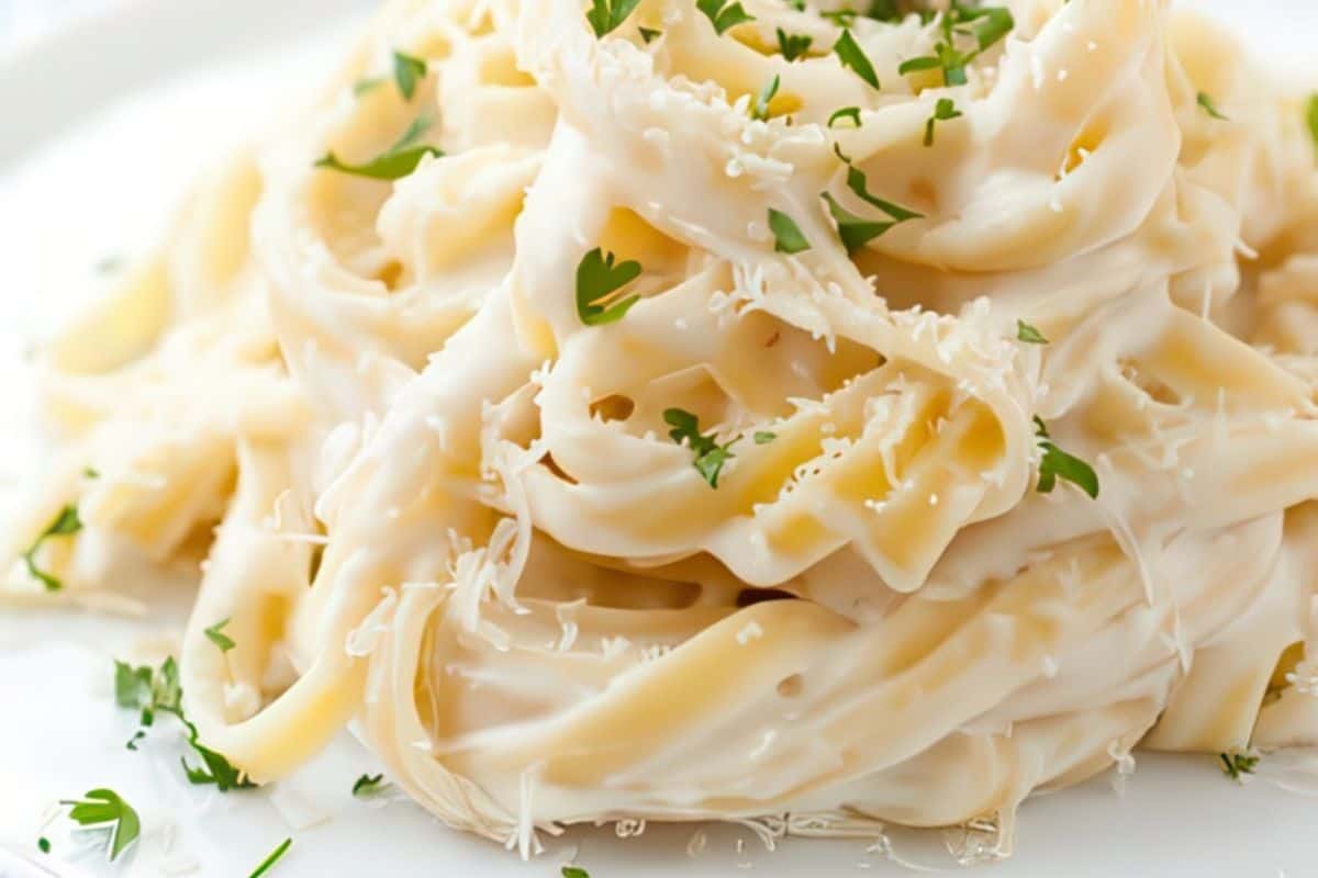 Fettuccine pasta coated in a creamy white sauce, topped with grated cheese and chopped parsley, served on a white plate.