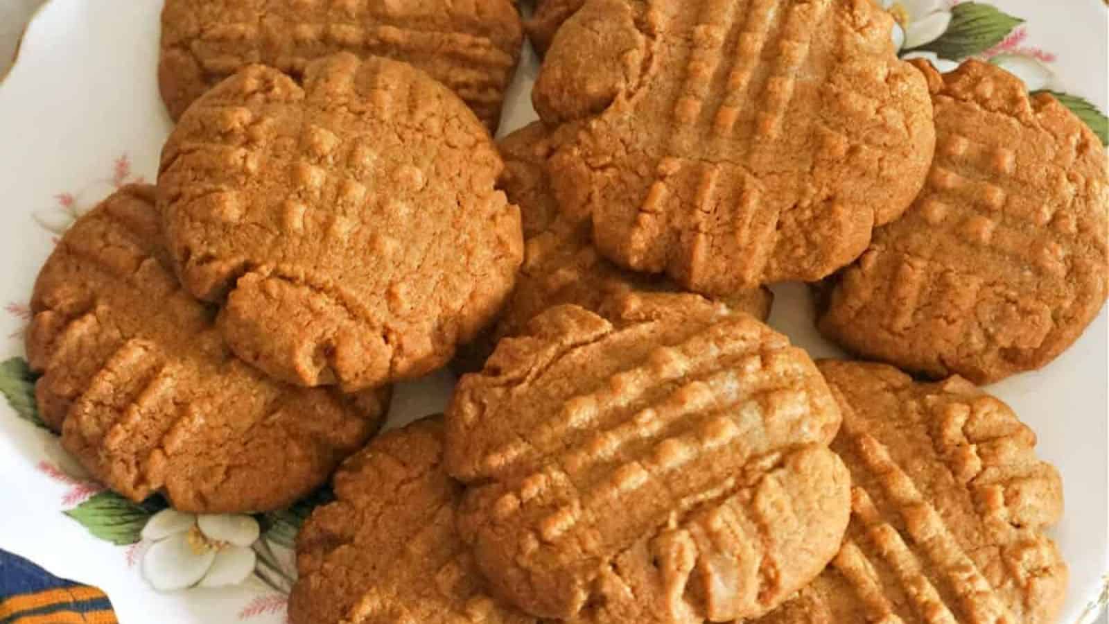 A group of round peanut butter cookies with crisscross fork marks on top, arranged closely together on a plate.