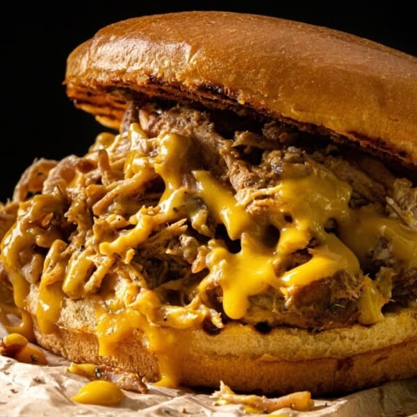 A pulled pork sandwich with melted cheese on a toasted bun, sitting on brown parchment paper.