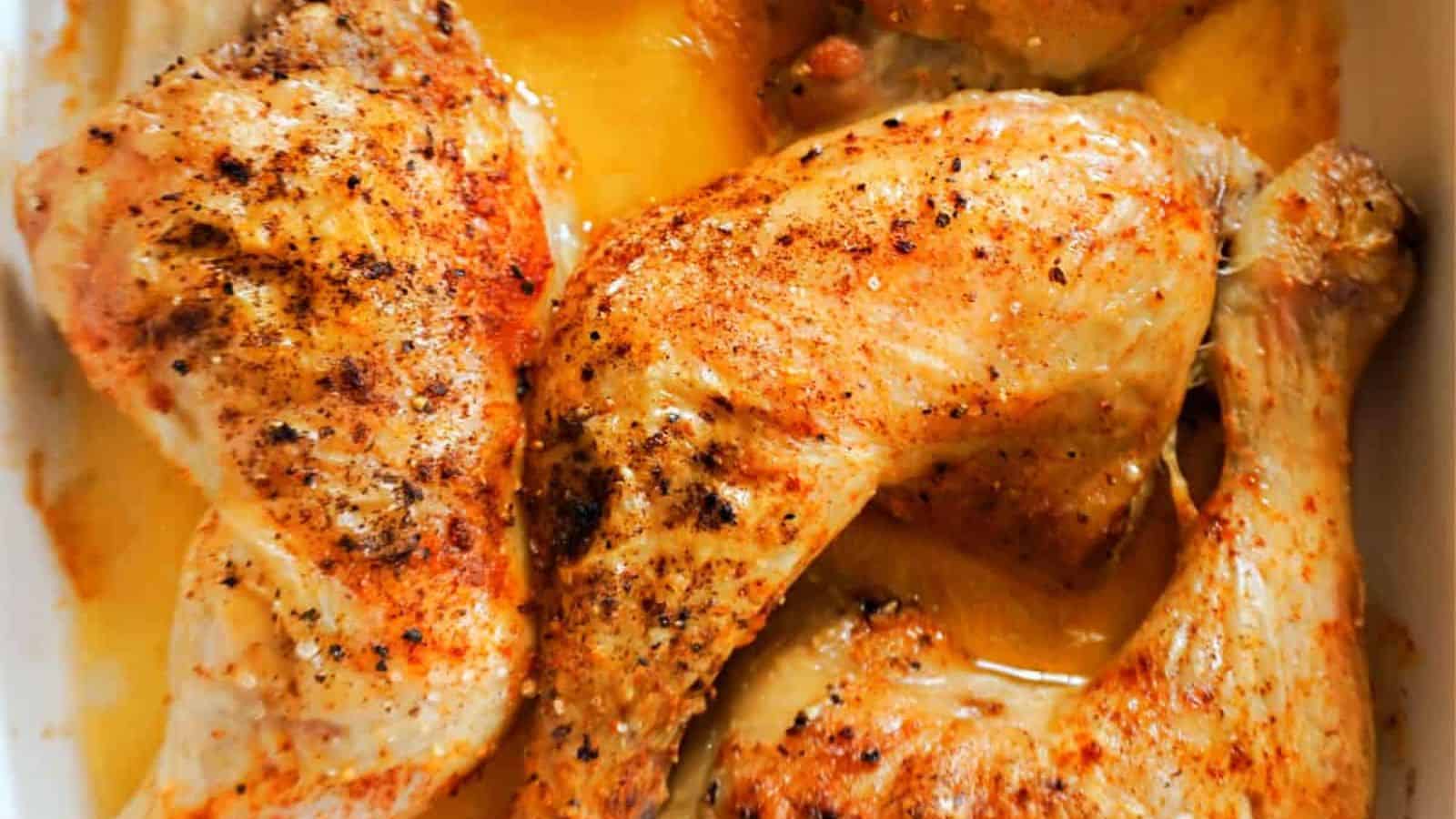 Chicken leg quarters with browned, seasoned skin, arranged in a white baking dish with golden juices at the bottom.