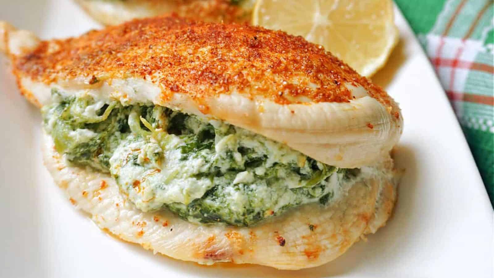Sliced cooked chicken breast with a creamy spinach and cheese filling, arranged on a white plate with a lemon slice in the background.