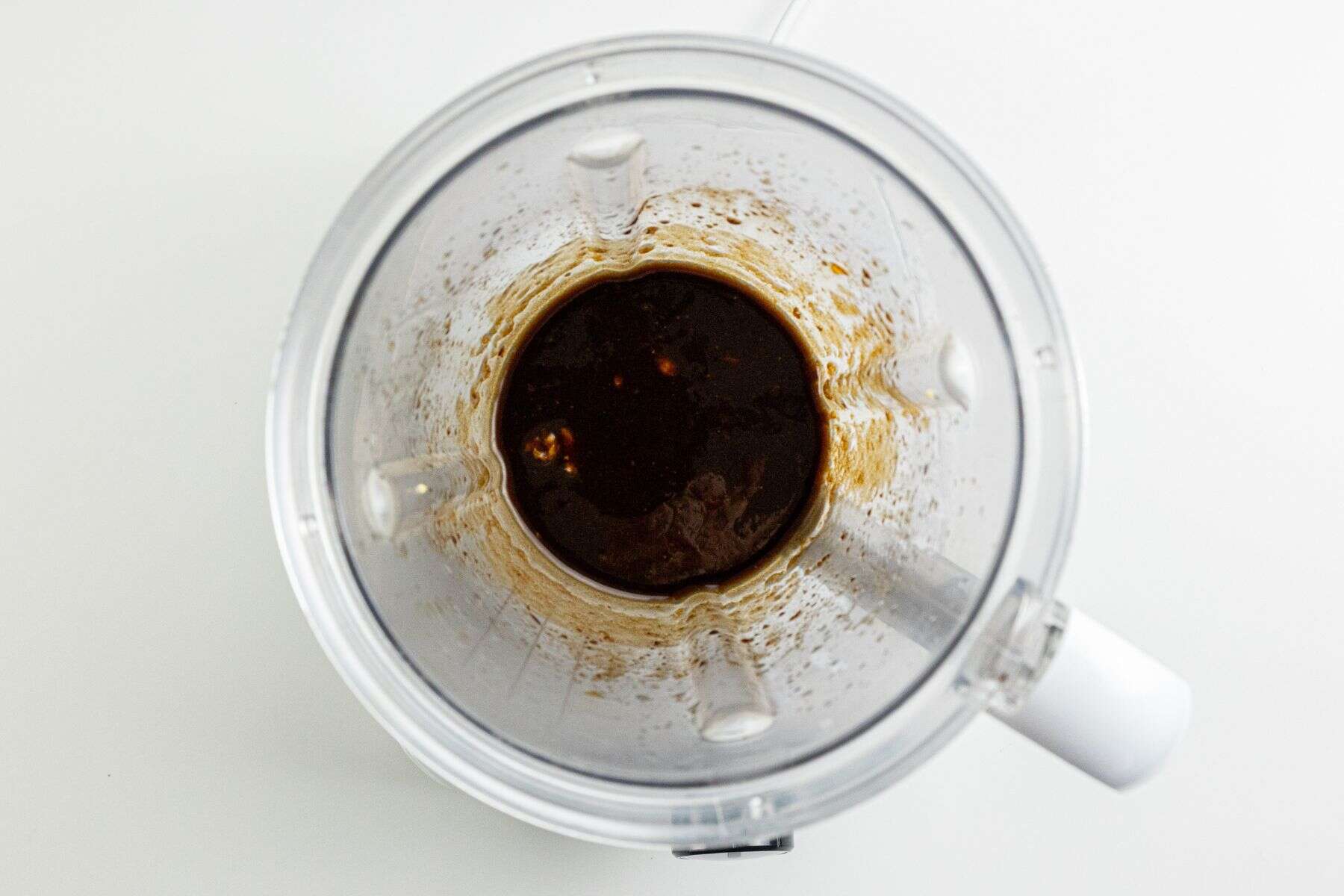 Top view of a blender with a dark brown liquid mixture and small chunks inside, placed on a white background.