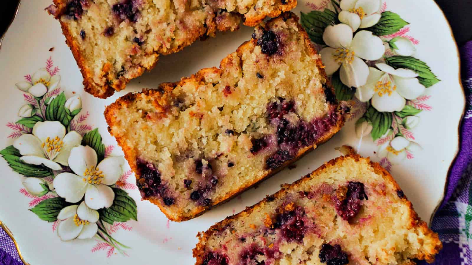 Three slices of berry loaf cake are arranged on a decorative plate featuring white floral designs.