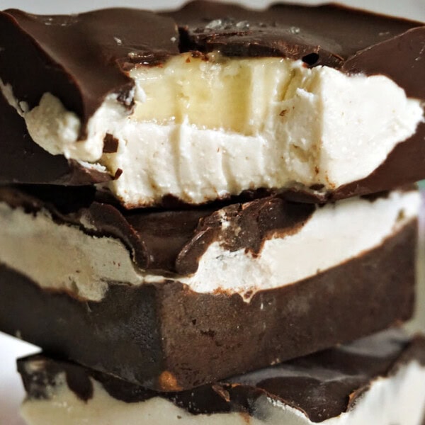 Three thick chocolate squares with creamy white filling are stacked; the top piece has a bite taken out, exposing the filling.