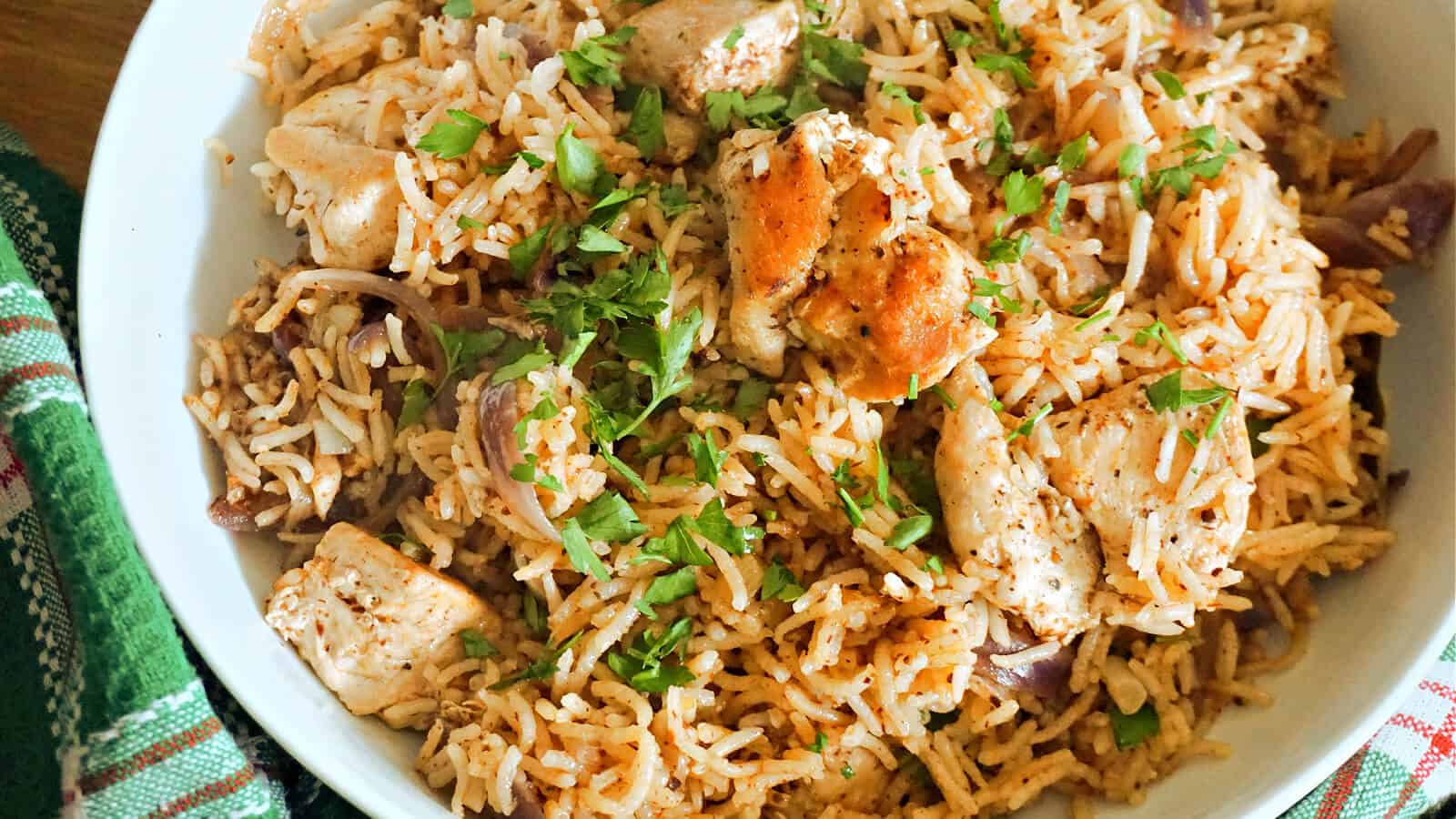A white plate holding a bowl of rice mixed with chicken breast pieces, chopped parsley, and sliced red onions.