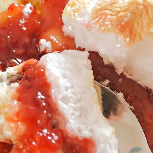 Close-up of a dessert with white meringue, yellow custard, and a layer of red jam or fruit sauce.