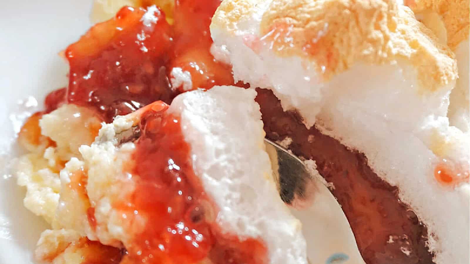 Close-up of a dessert with white meringue, yellow custard, and a layer of red jam or fruit sauce.