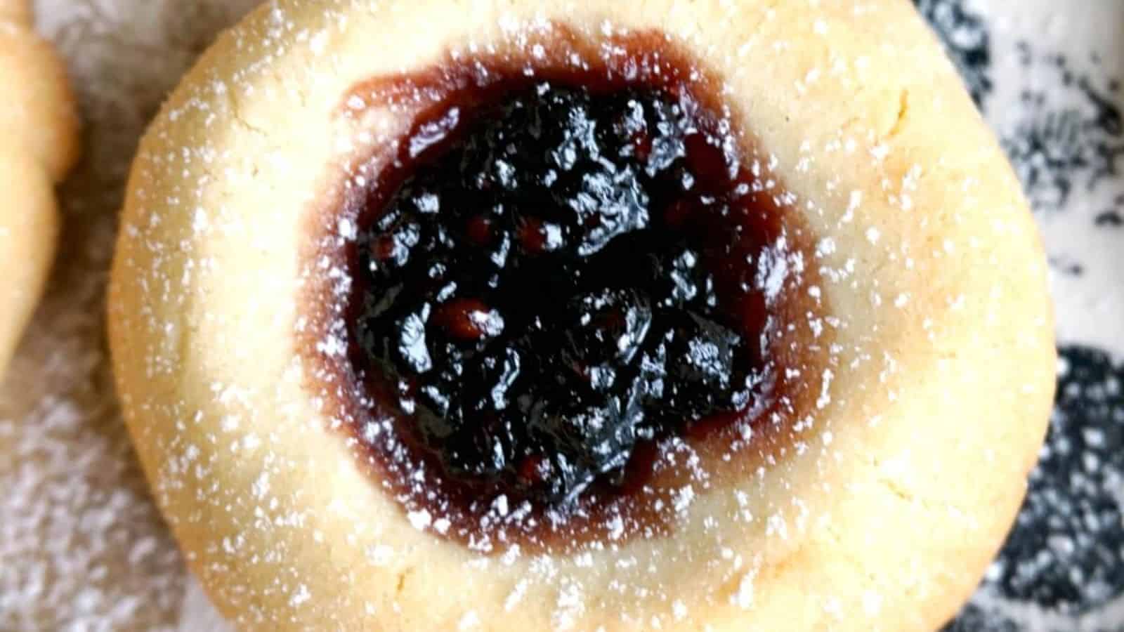 A round cookie with a center filled with dark berry jam, dusted with powdered sugar.