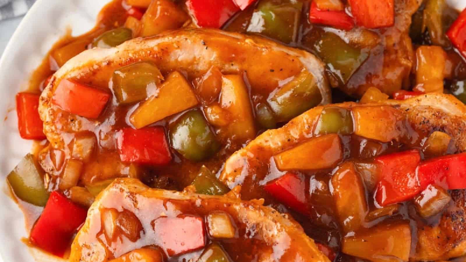 Cooked pork chops topped with a glossy brown sauce, diced red and green bell peppers, and pineapple pieces.