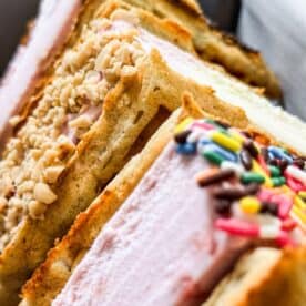 Waffle ice cream sandwiches made with vanilla wafers, some coated in chopped nuts and others in colorful sprinkles.