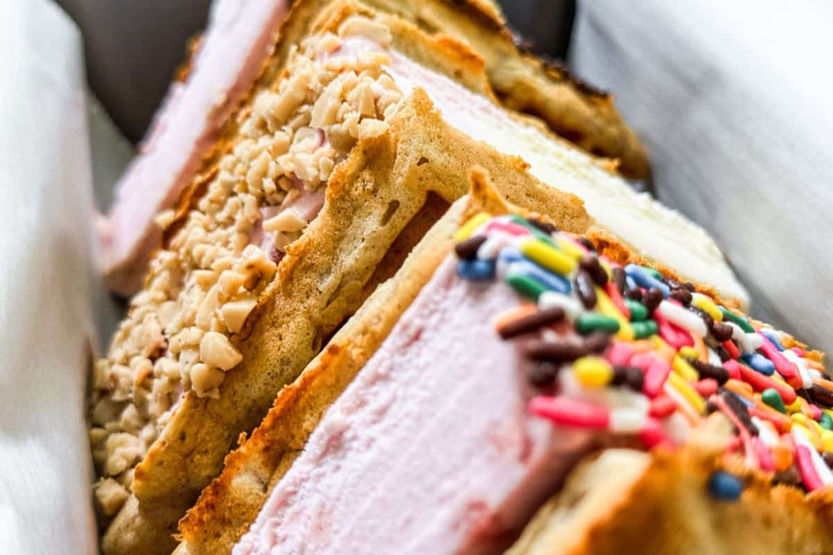 Waffle ice cream sandwiches made with vanilla wafers, some coated in chopped nuts and others in colorful sprinkles.