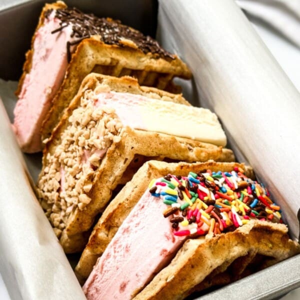 Waffle ice cream sandwiches topped with assorted sprinkles and toppings are arranged in a metal tray.