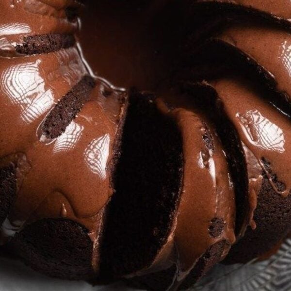 A chocolate bundt cake with a glossy chocolate glaze, sliced and set on parchment paper.