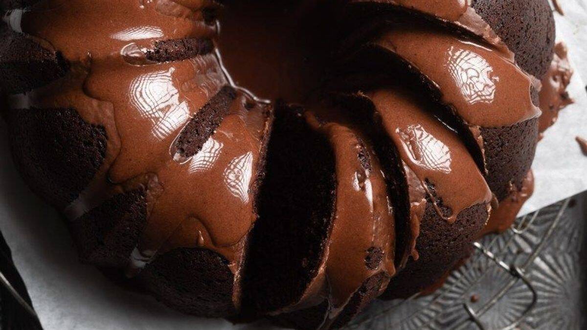 A chocolate bundt cake with a glossy chocolate glaze, sliced and set on parchment paper.