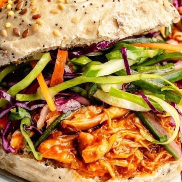 A seeded bun filled with shredded barbecue chicken and colorful coleslaw.