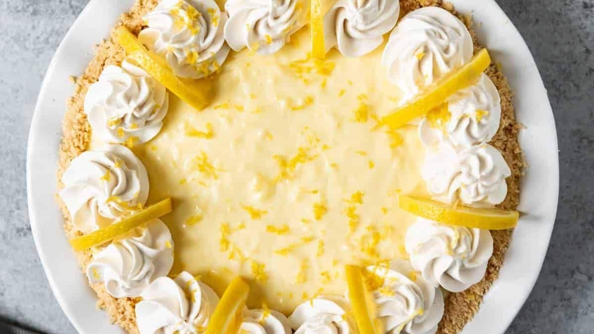 A lemon pie on a white plate, garnished with whipped cream, lemon zest, and slices of lemon.