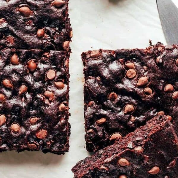 Squares of chocolate chip brownies arranged on a white surface, with a knife positioned beside them.
