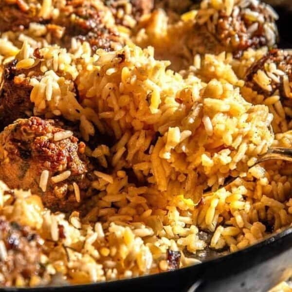 A skillet filled with yellow rice and browned meatballs, with a spoon scooping up the rice.
