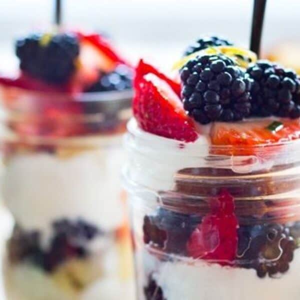 Two glass jars containing layers of yogurt, blackberries, strawberries, and granola, each with a spoon.