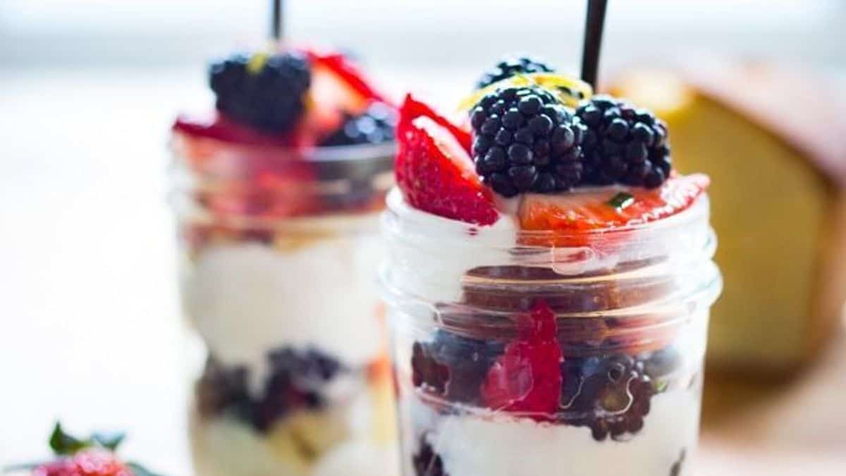 Two glass jars containing layers of yogurt, blackberries, strawberries, and granola, each with a spoon.