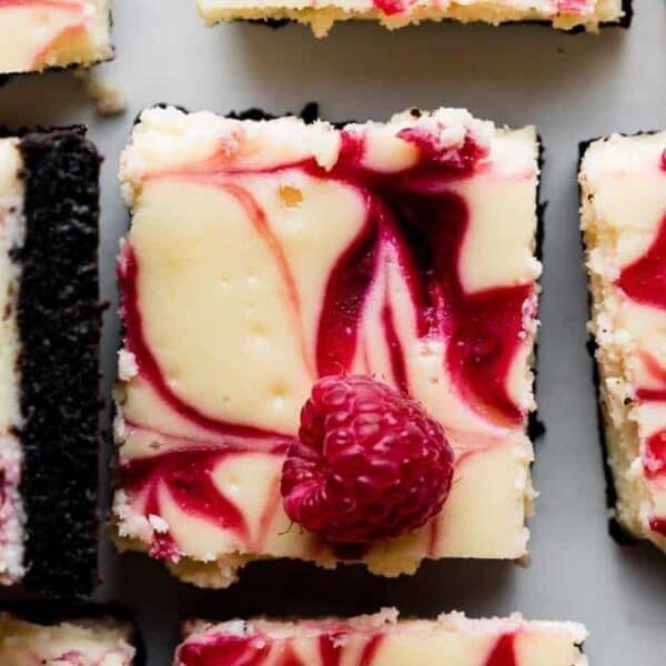 Top view of cheesecake bars with a raspberry swirl and cookie crust; one bar is topped with a single raspberry.