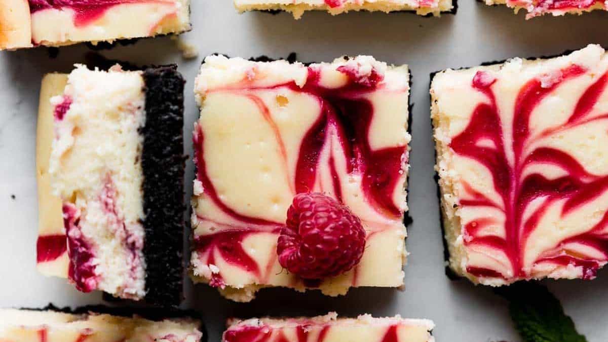 Top view of cheesecake bars with a raspberry swirl and cookie crust; one bar is topped with a single raspberry.
